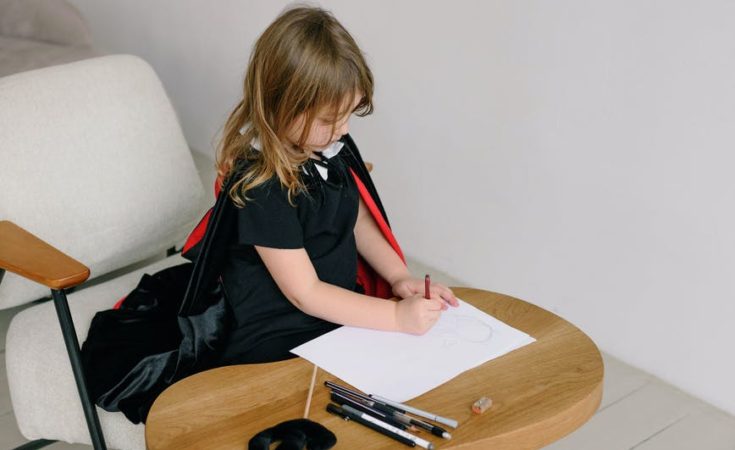a girl in black dress sitting on white chair while drawing on white paper